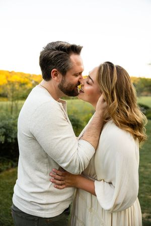 A tender moment between a couple wearing light colored sweaters against a golden sunset backdrop.