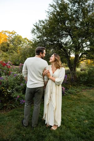 A couple shares a tender moment together on a grassy hill surrounded by blooming flowers at sunset.