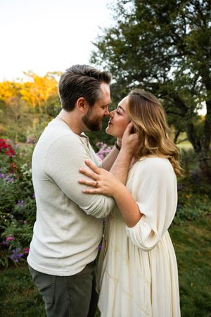 A couple shares romantic embraces in a garden setting during autumn with colorful foliage in the background.
