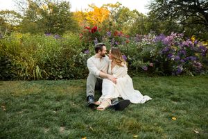 A romantic couple sits together in a lush garden with vibrant autumn flowers and foliage at sunset.