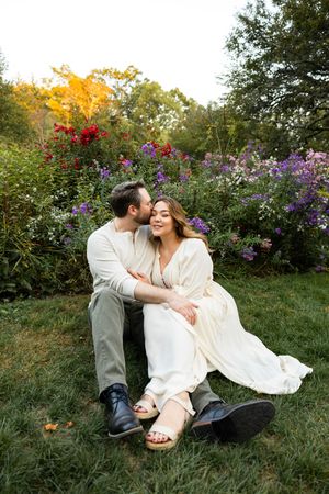 A couple laughs together while sitting in a garden filled with colorful wildflowers during golden hour.