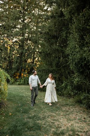 A couple walks together through a lush green garden during golden hour.