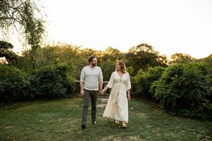A couple walks together in a scenic garden setting during golden hour at sunset.