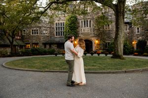 A couple shares a romantic moment in front of a stone building at dusk.