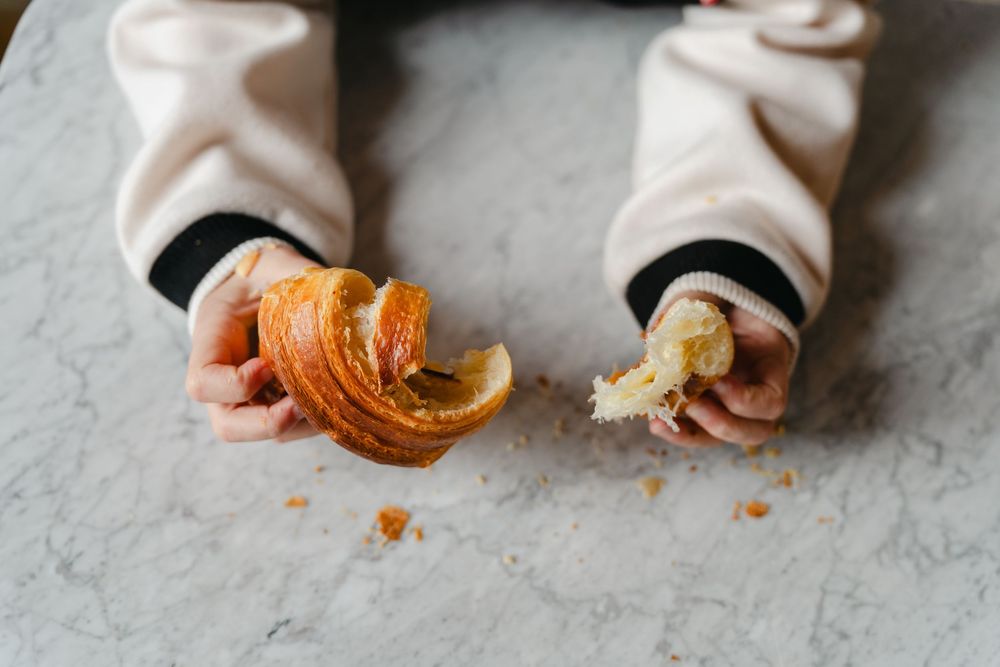Small hands holding and examining a fresh orange mandarin or clementine on a light gray surface.