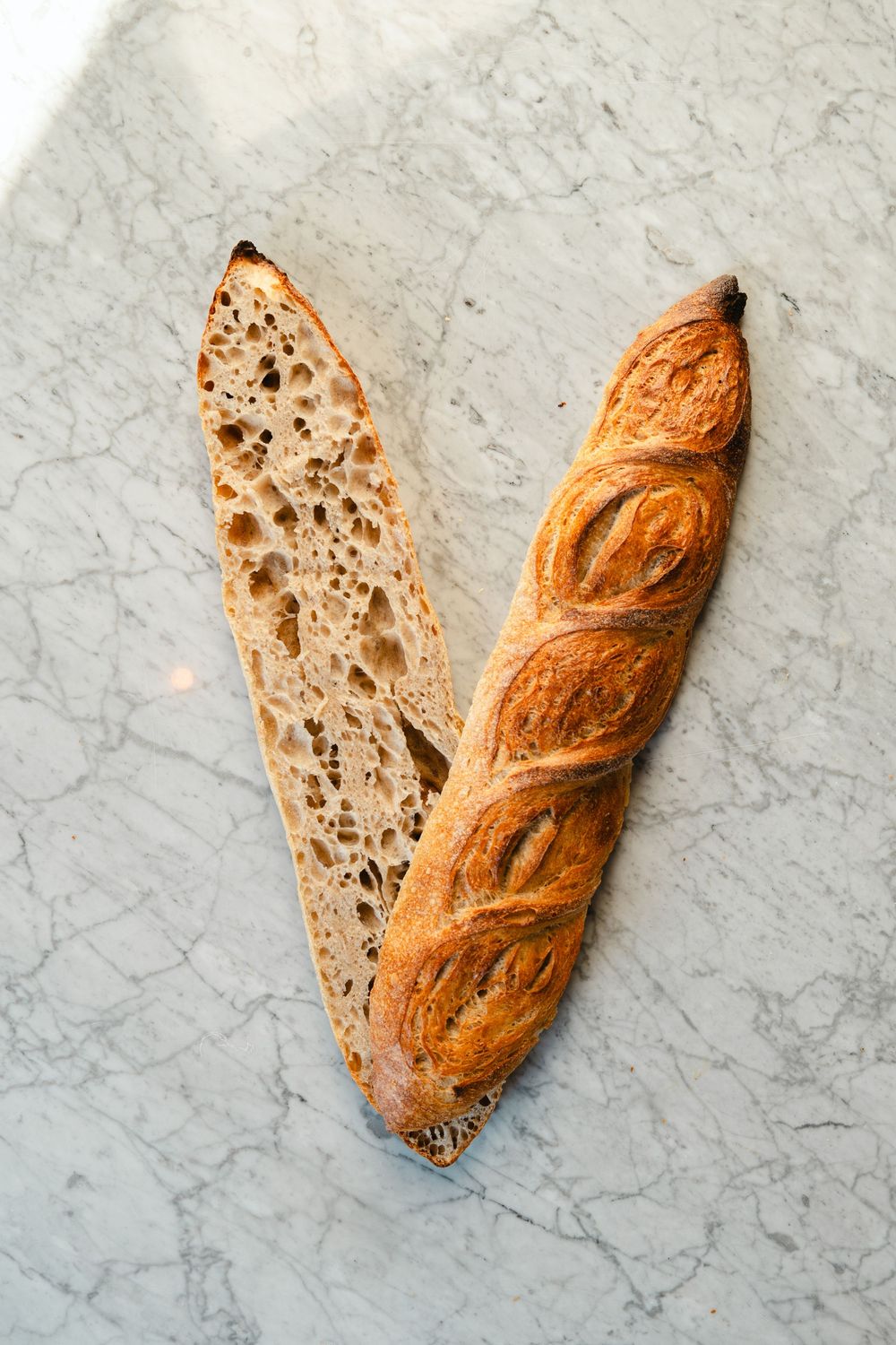 Sliced artisanal French baguette showing crusty exterior and airy interior crumb structure on marble surface.