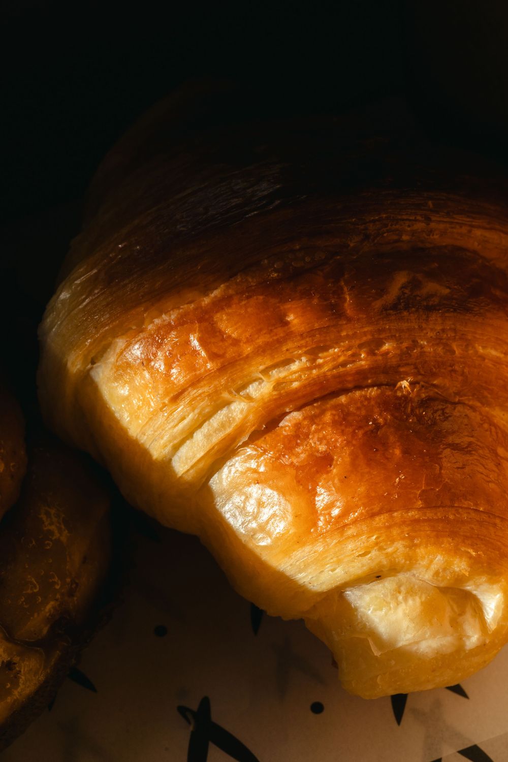 Close-up view of golden brown croissant crust showing flaky layers and buttery texture in warm lighting.