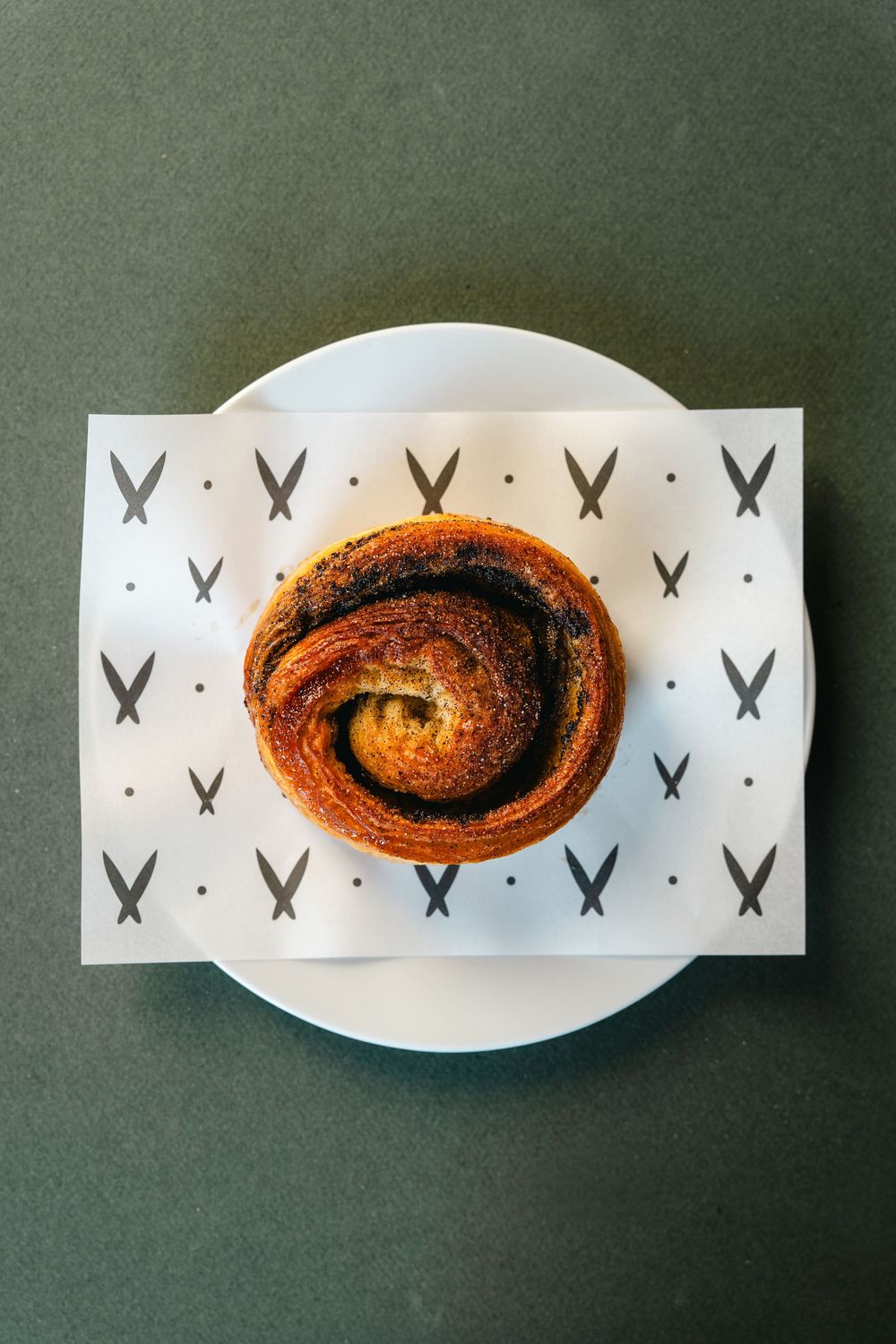 A cinnamon roll pastry served on a white plate with decorative butterfly pattern paper underneath.