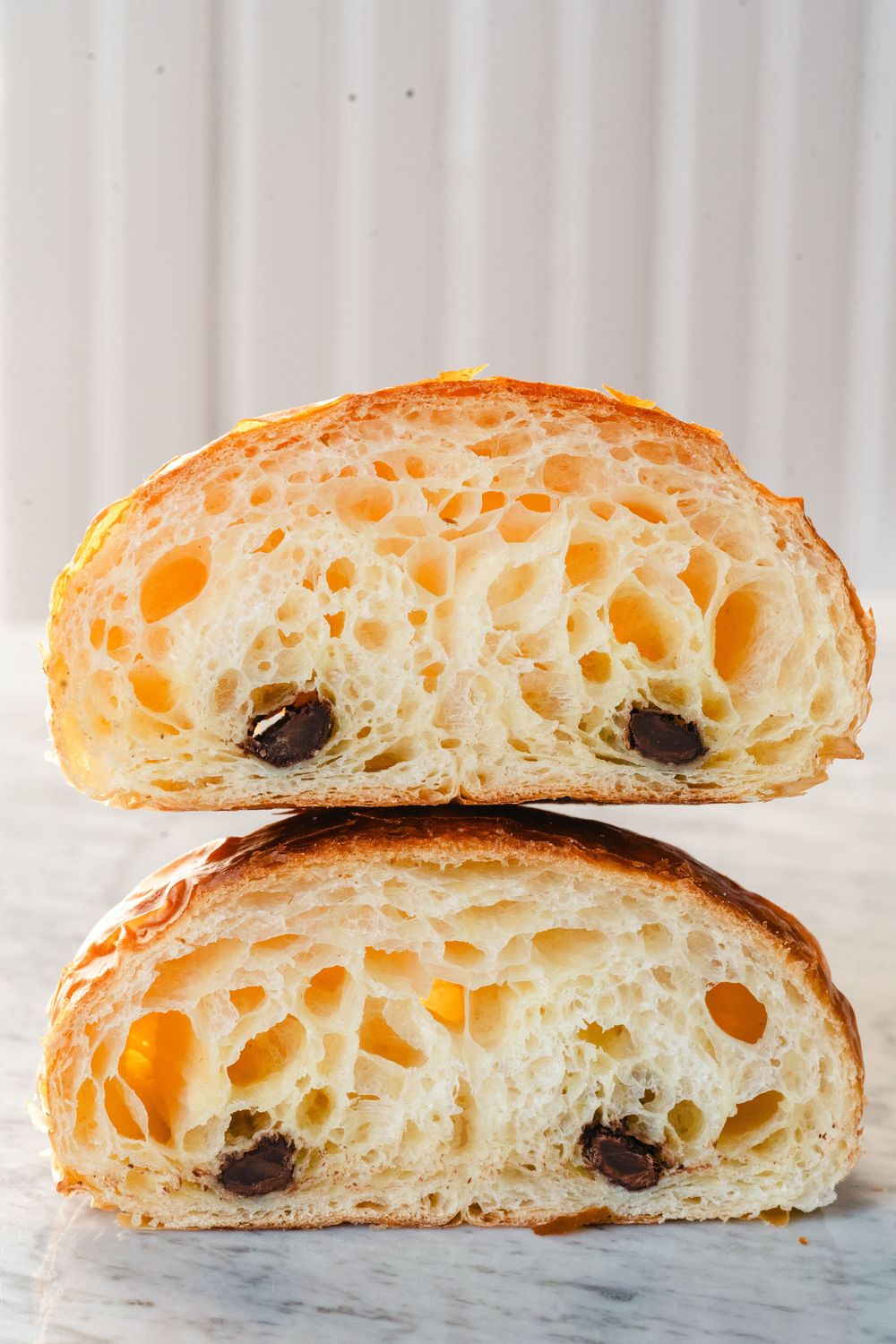Cross section of chocolate croissants showing airy honeycomb texture and dark chocolate pieces inside.