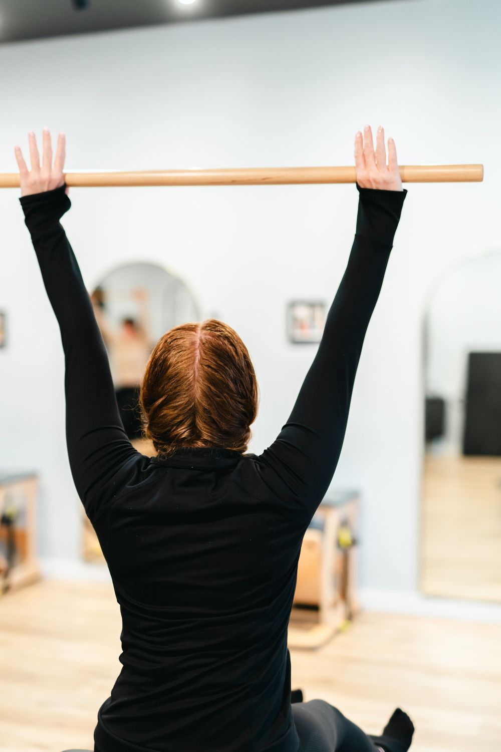 A person in black clothing practicing wall handstands with a wooden dowel for balance training.
