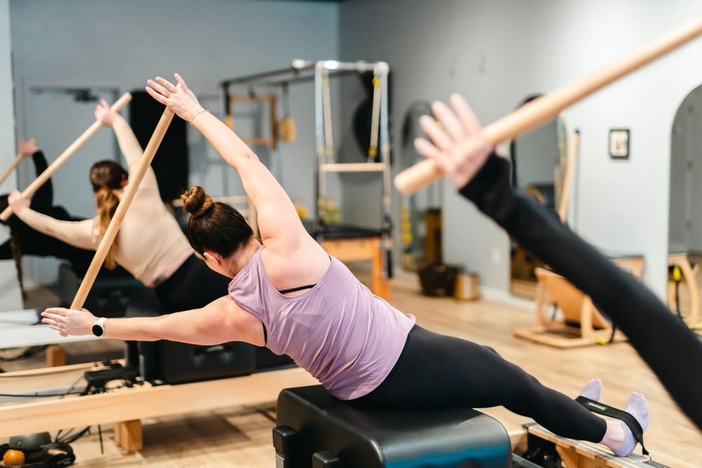 People practicing Pilates exercises on reformer machines in a bright fitness studio.