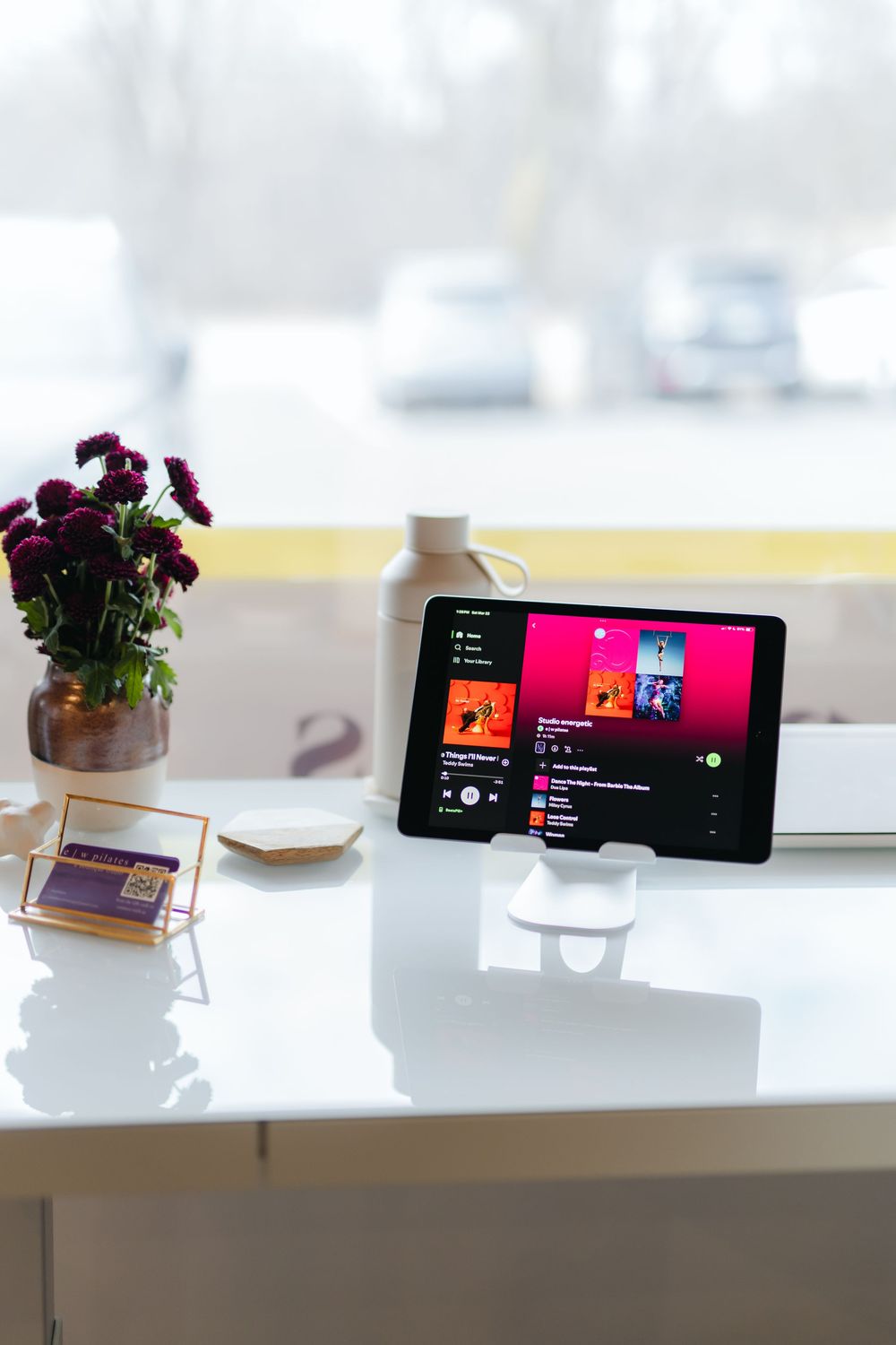 A modern white desk setup with a smartphone displaying music and a small potted plant for decoration.