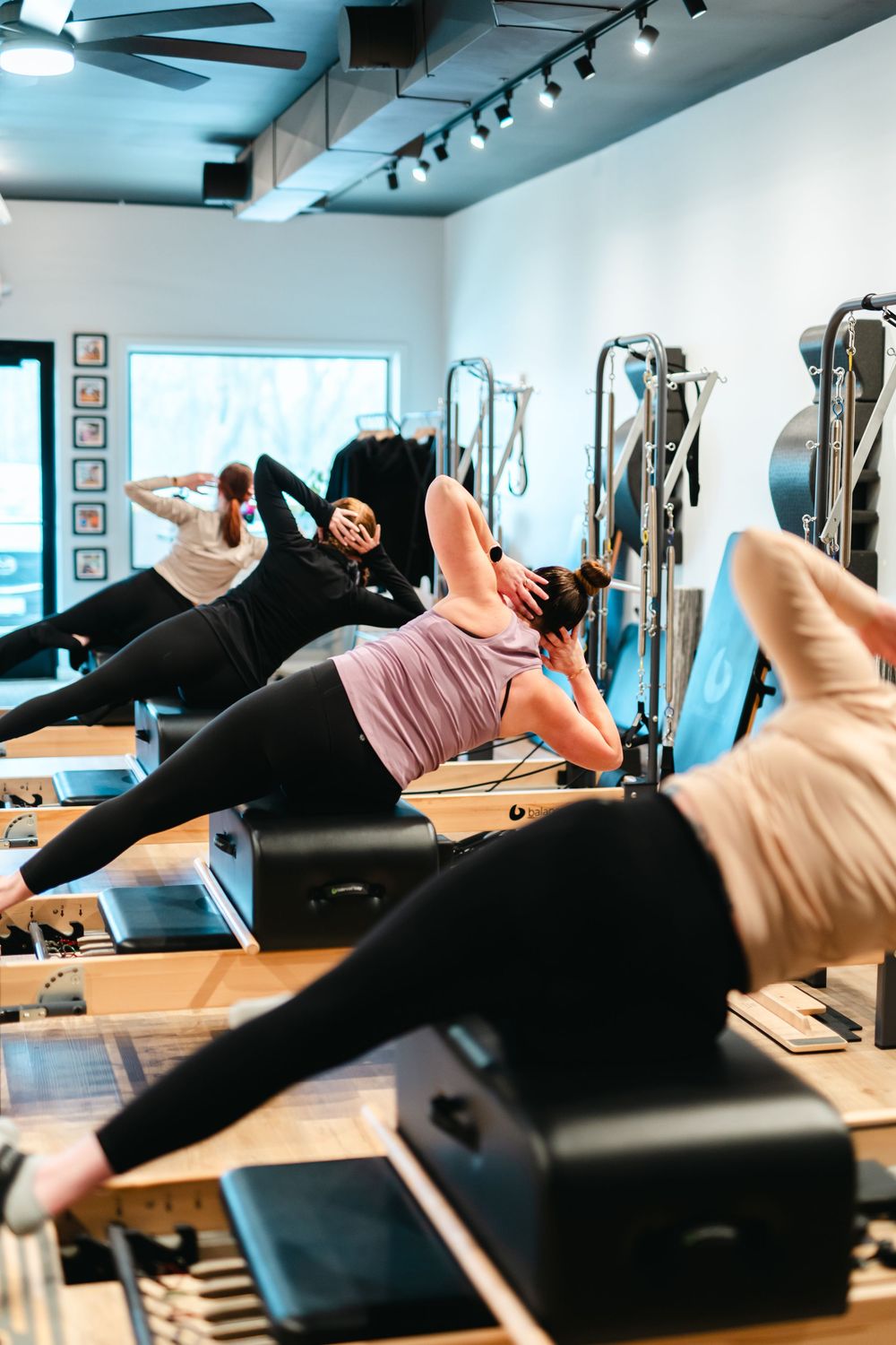 People practicing Pilates exercises on reformer machines in a bright, modern fitness studio.