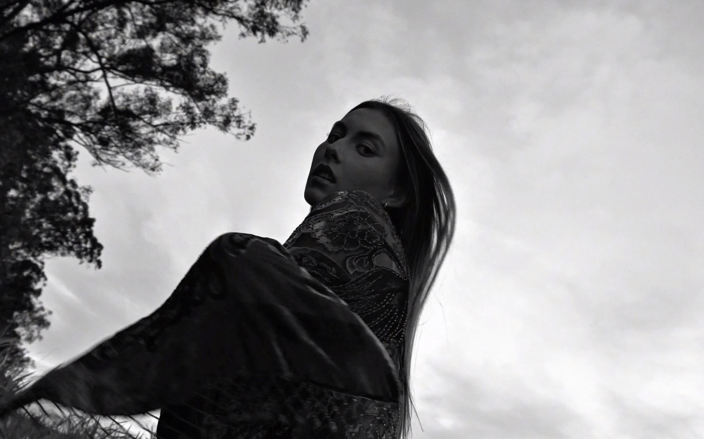 A black and white artistic photograph shows a figure in motion against a dramatic cloudy sky.
