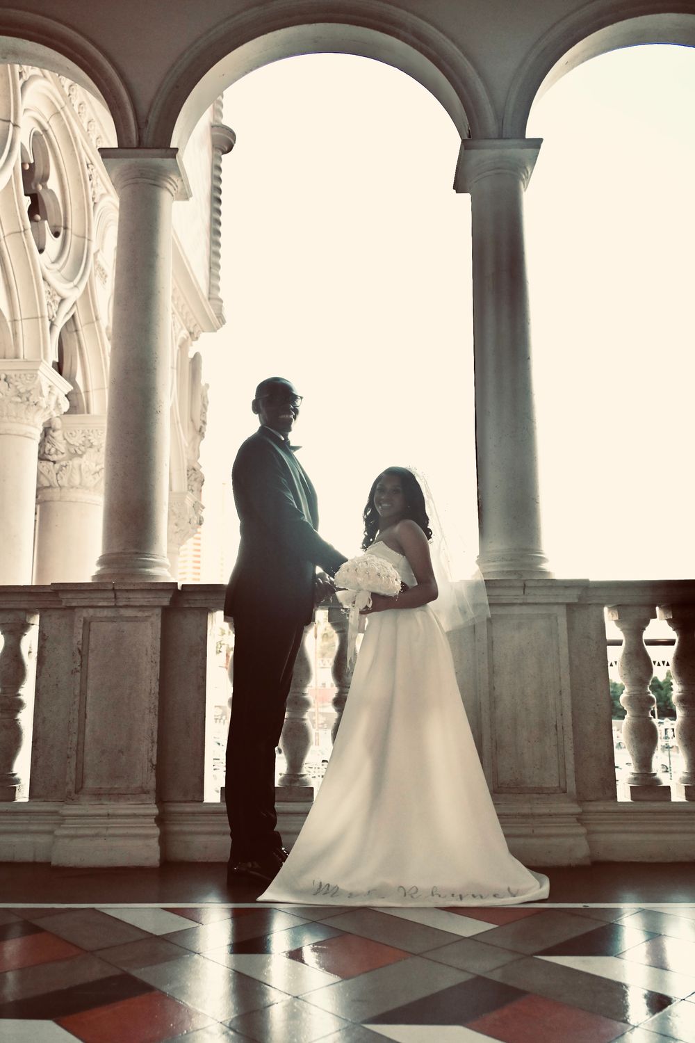 Bride and groom silhouetted in elegant arched marble hallway during wedding photo session.