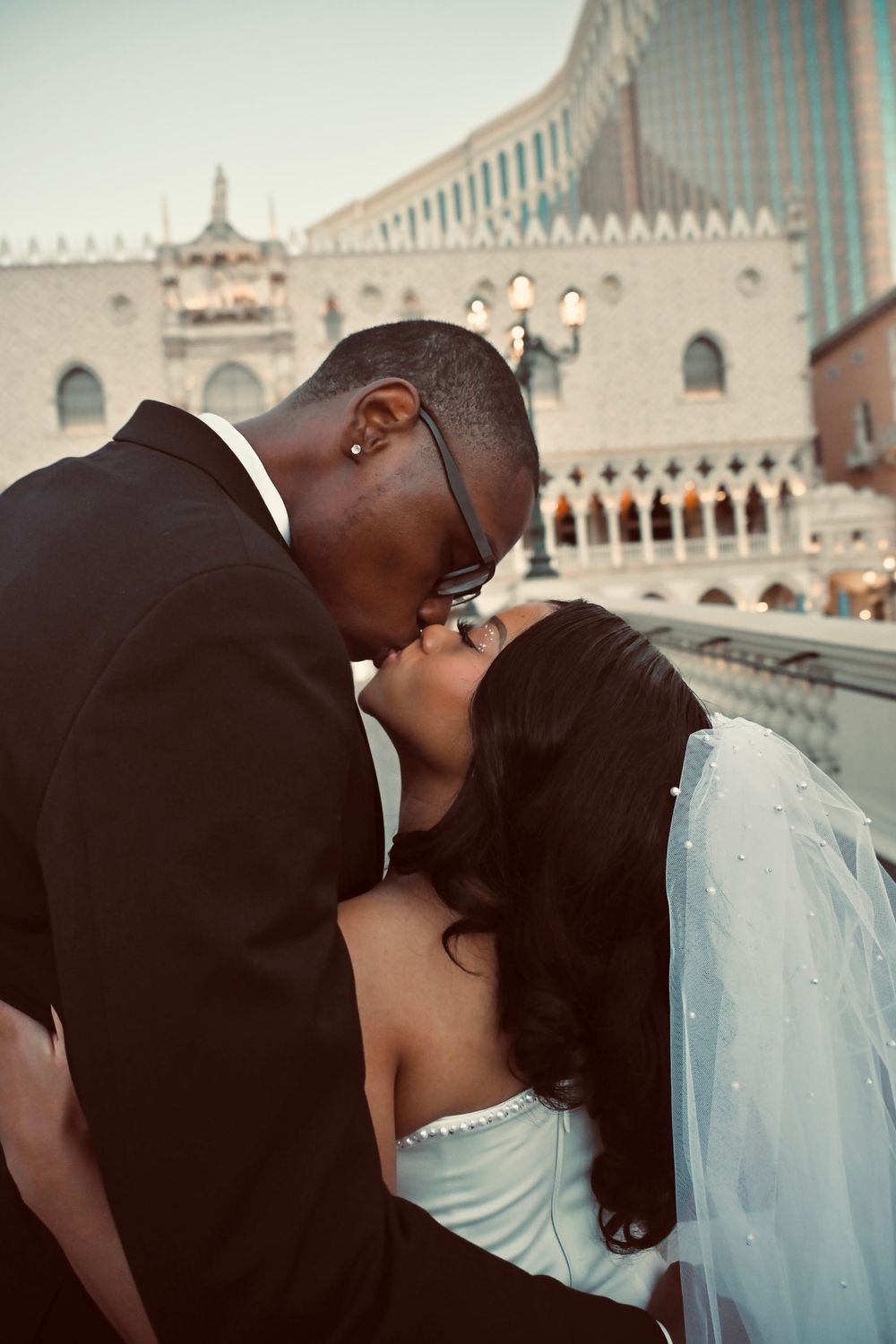 Black newlyweds share a romantic kiss in wedding attire with The Venetian Las Vegas resort in the background.