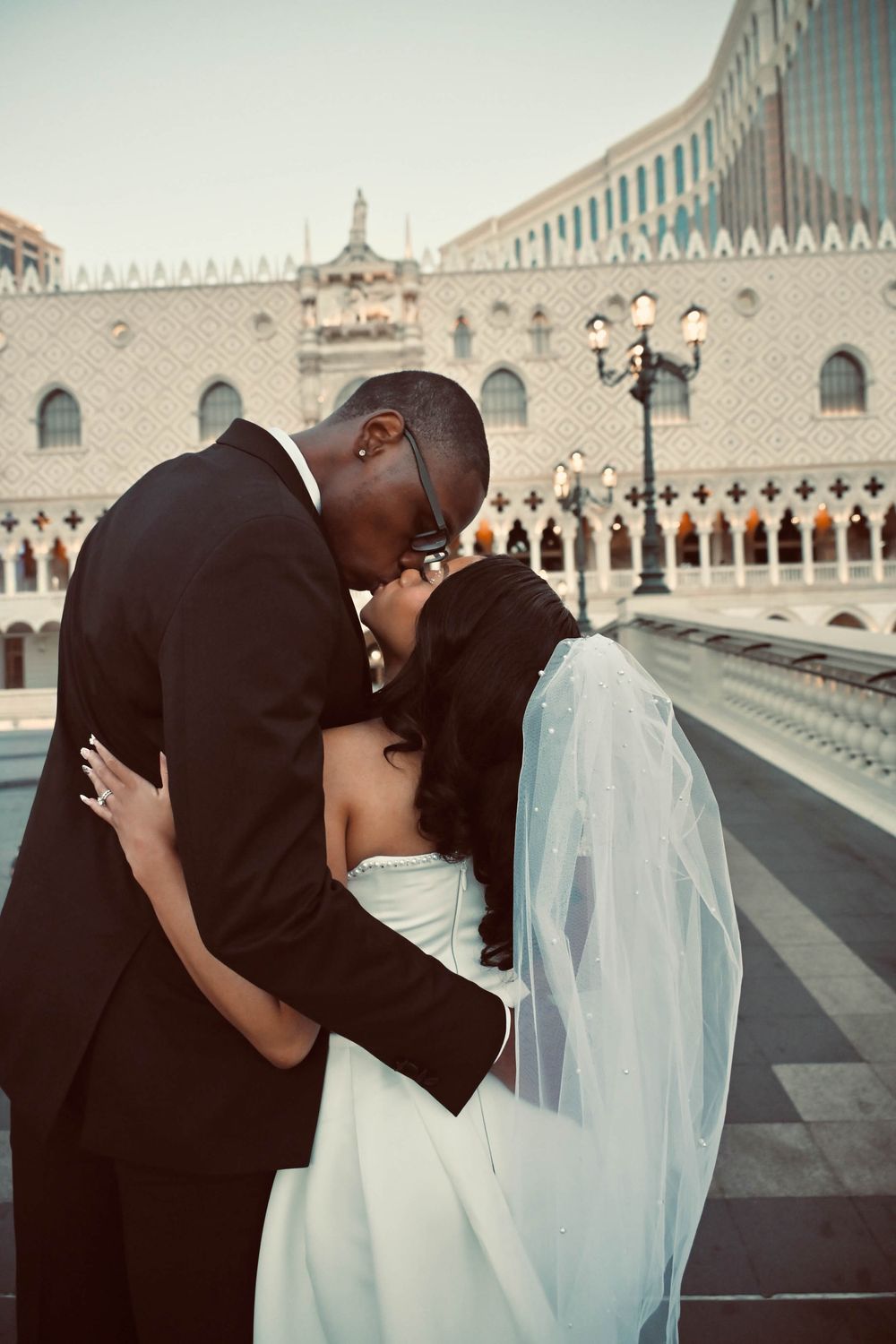 Newlywed couple sharing a romantic kiss outside The Venetian Las Vegas in wedding attire.