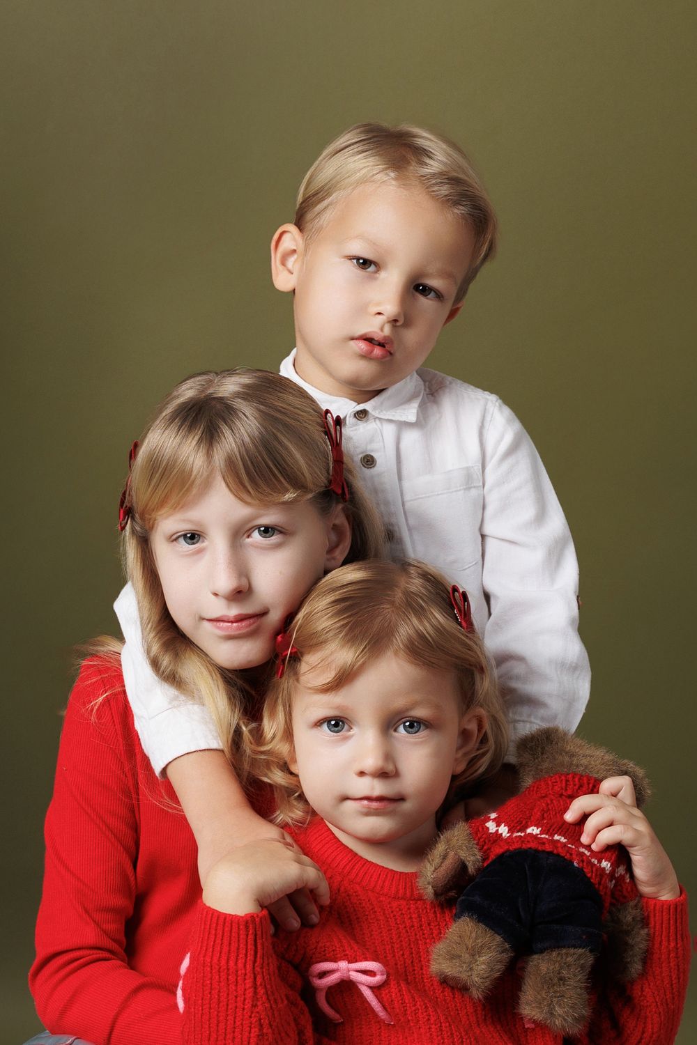 A series of five connected portrait photos showing siblings in red and white outfits against an olive green background.