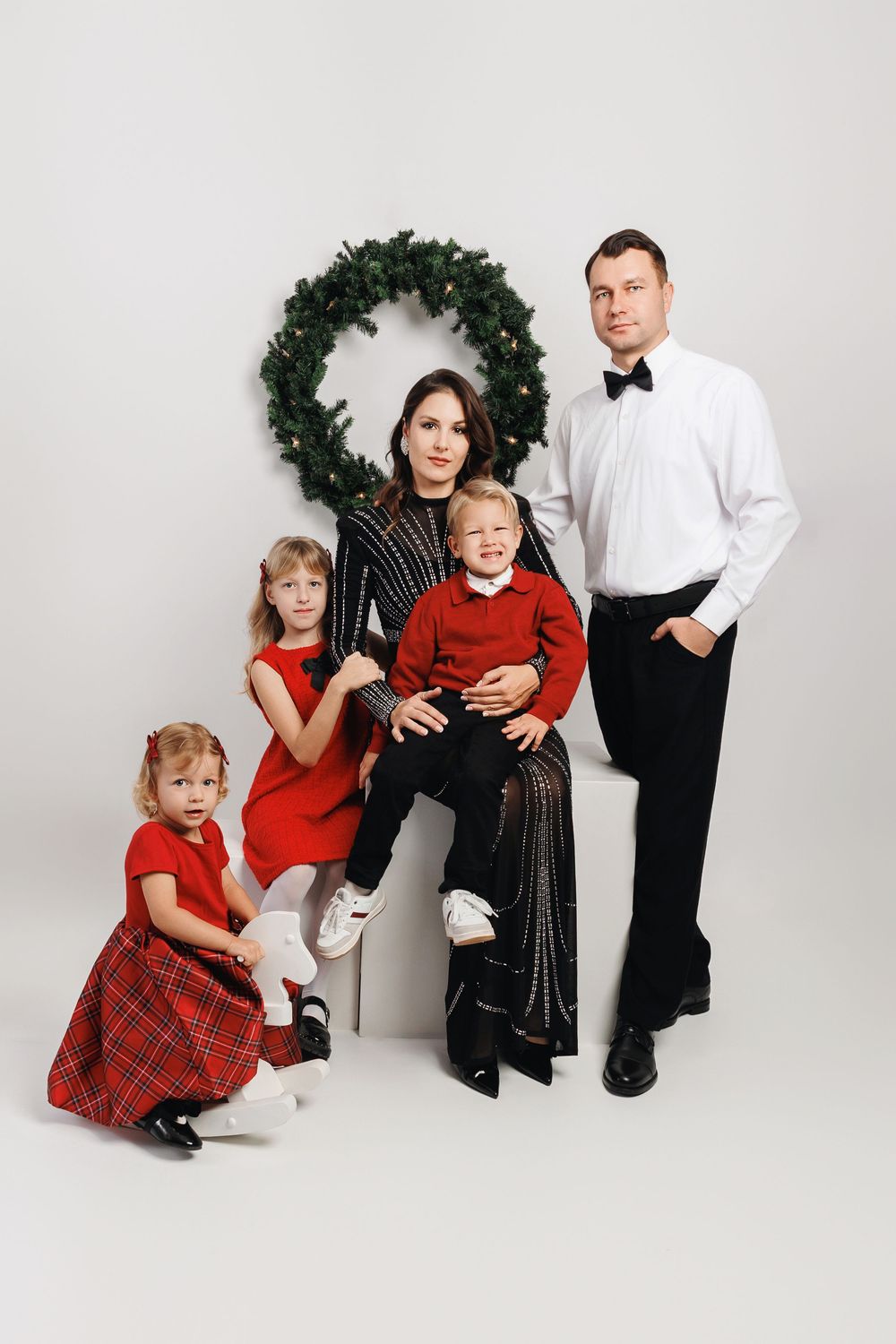 Professional studio portrait session showing family members in coordinated red and black formal attire against white backdrop.