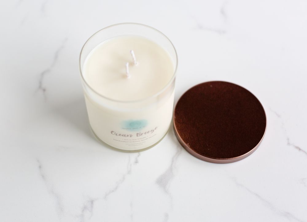 Minimalist white candle with brown lid shown on white marble background.