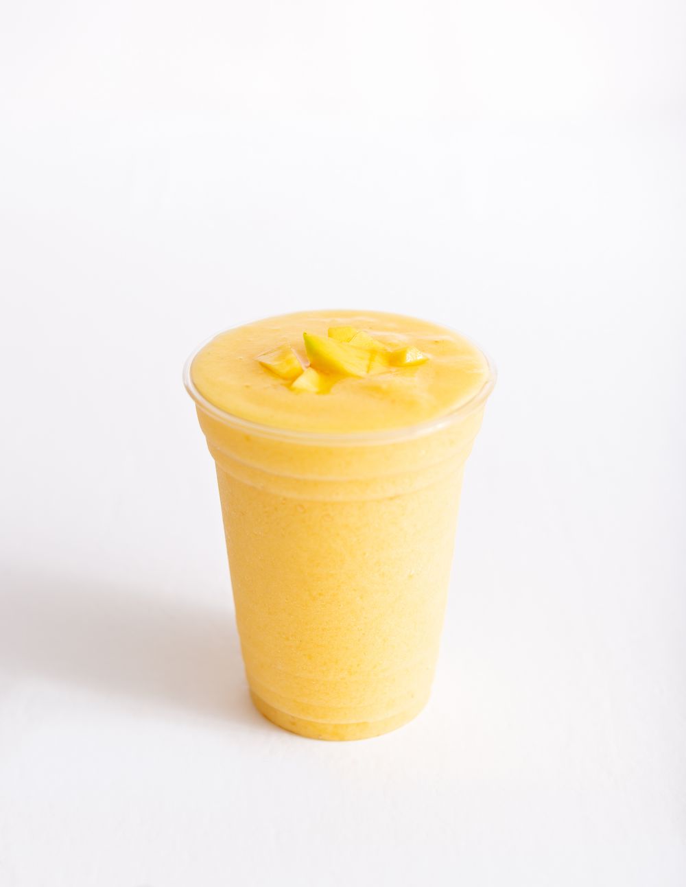 Bright yellow mango smoothie in a clear plastic cup against white background.
Brand, product photography.
