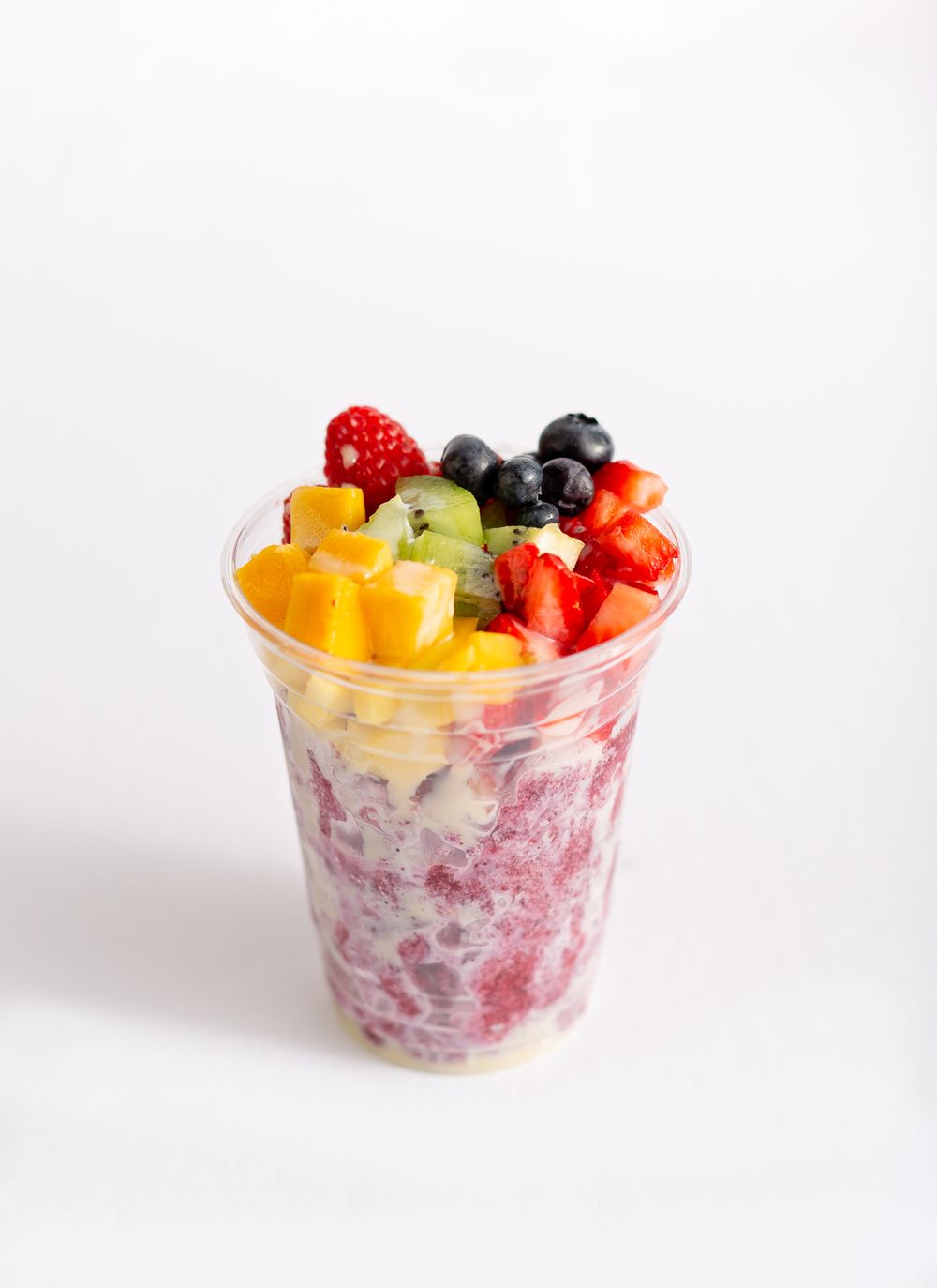 Colorful fruit parfait with berries, mango and yogurt in a clear plastic cup.
Brand, product photography.