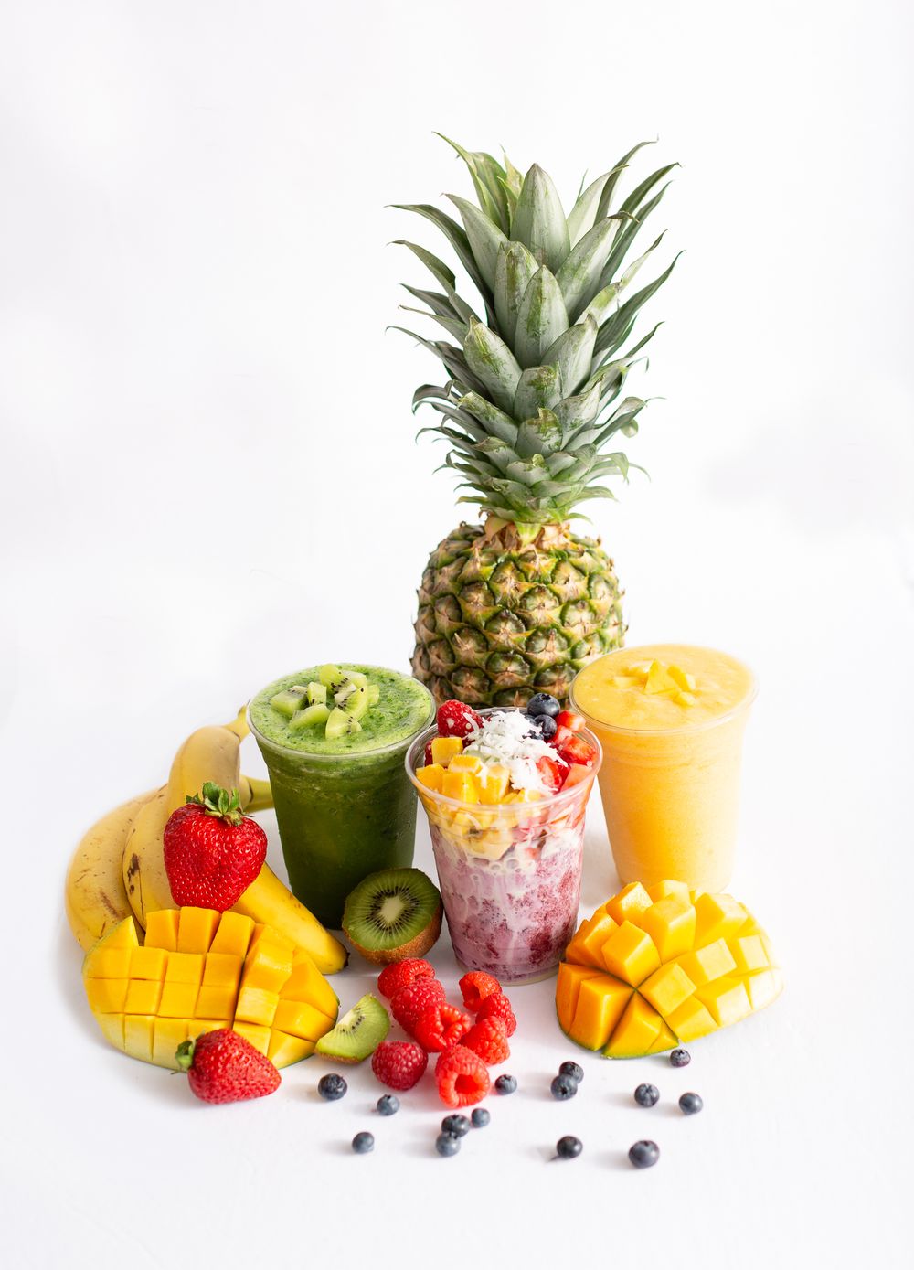 Fresh tropical fruits and smoothies arranged with pineapple, mango, and berries on white background.
Brand, product photography.