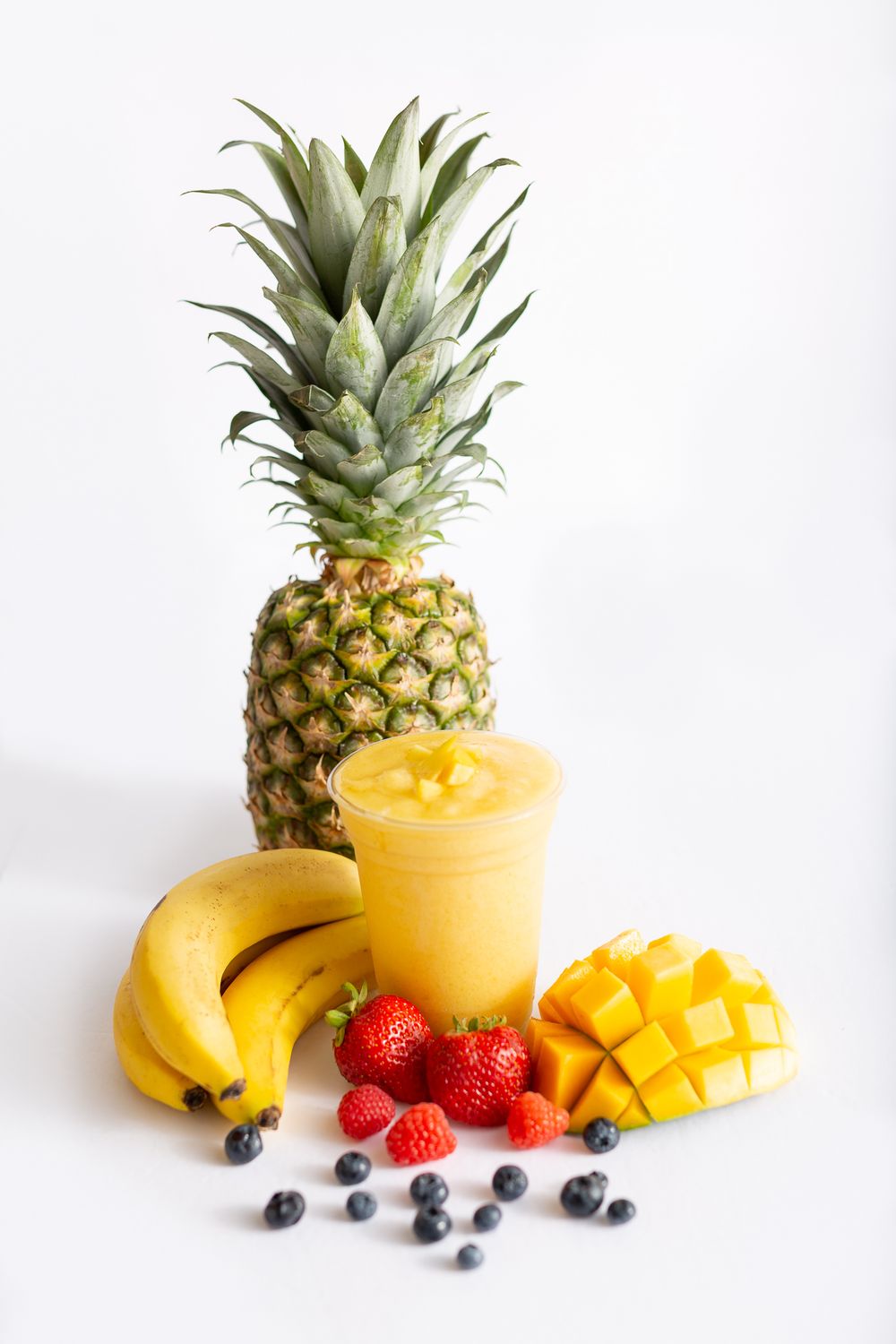 Tropical smoothie ingredients with pineapple, bananas, mango and berries on white background.
Brand, product photography.