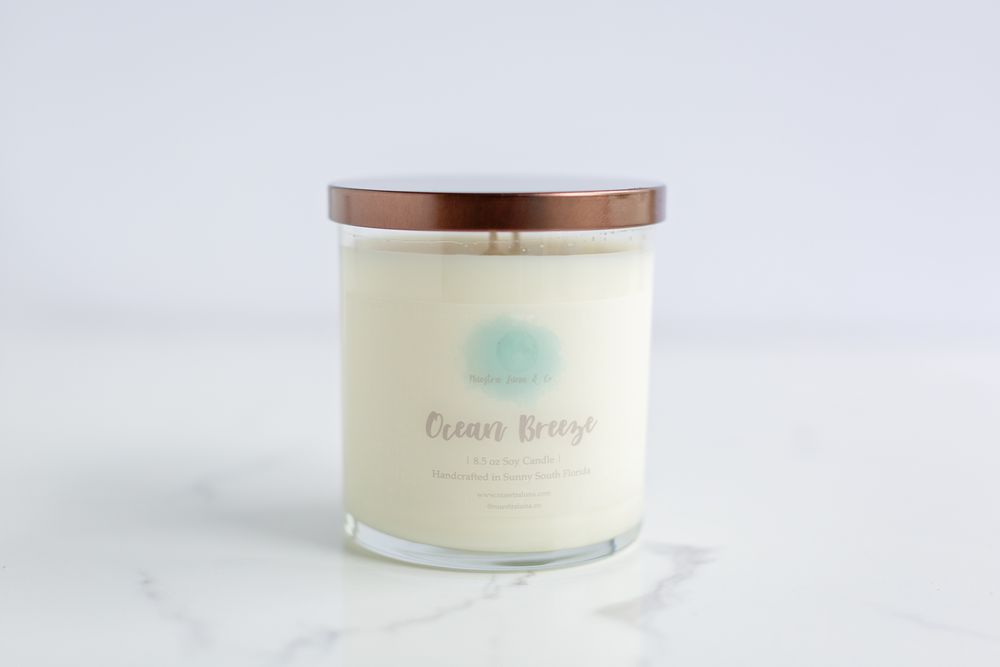 White candle in a glass jar with copper lid displayed on marble surface.