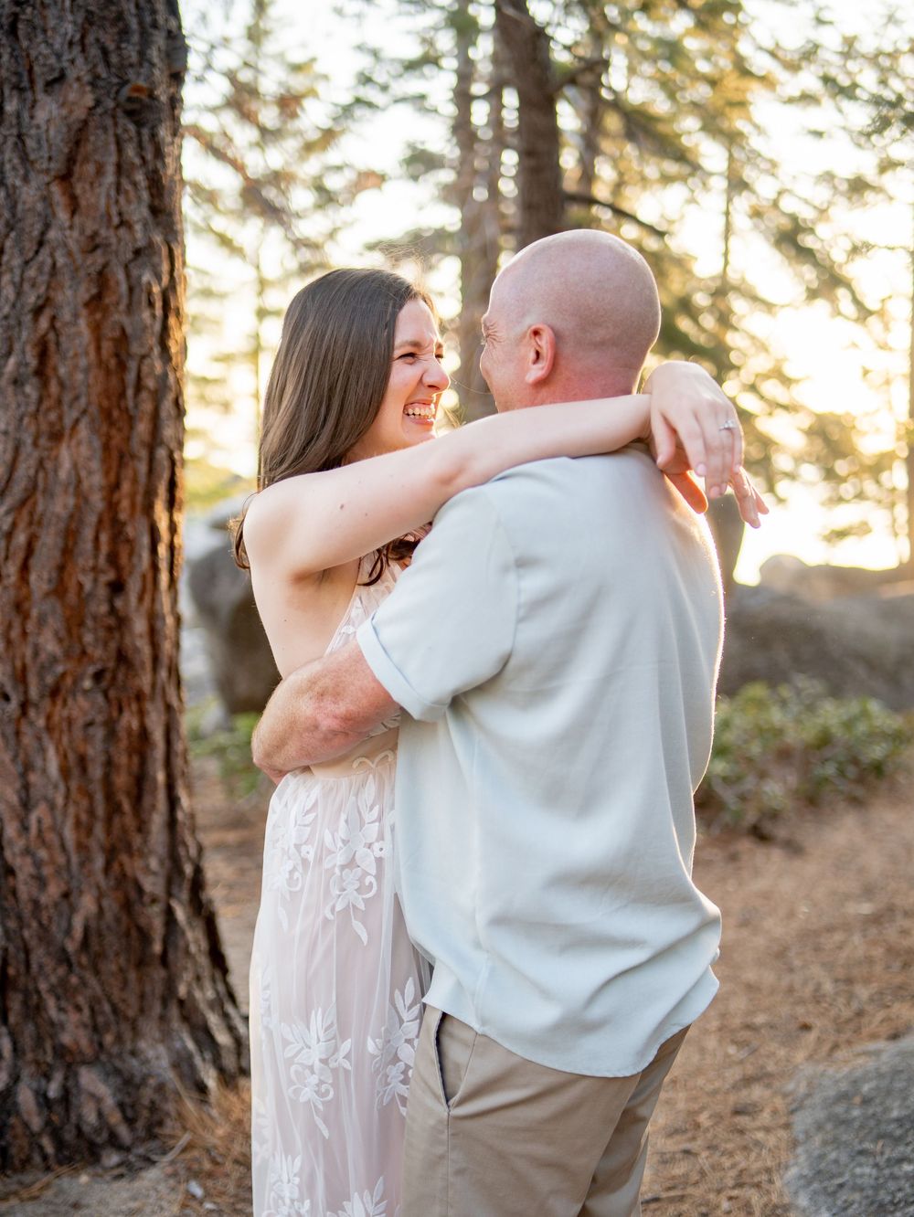 A romantic couple dances together among tall pine trees during a sunset photo session.