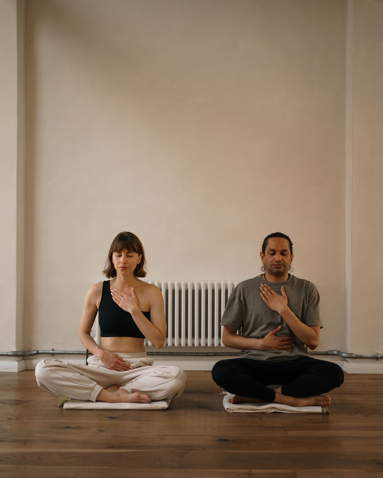 A time-lapse sequence shows two people sitting on wooden floor practicing meditation and deep breathing exercises.