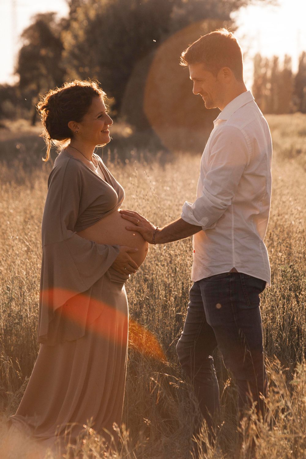 coppia uomo e donna incinta, mano sulla pancia, luce tramonto, campo di spighe, luglio, caldo, amore, innamorati, sessione maternity materna