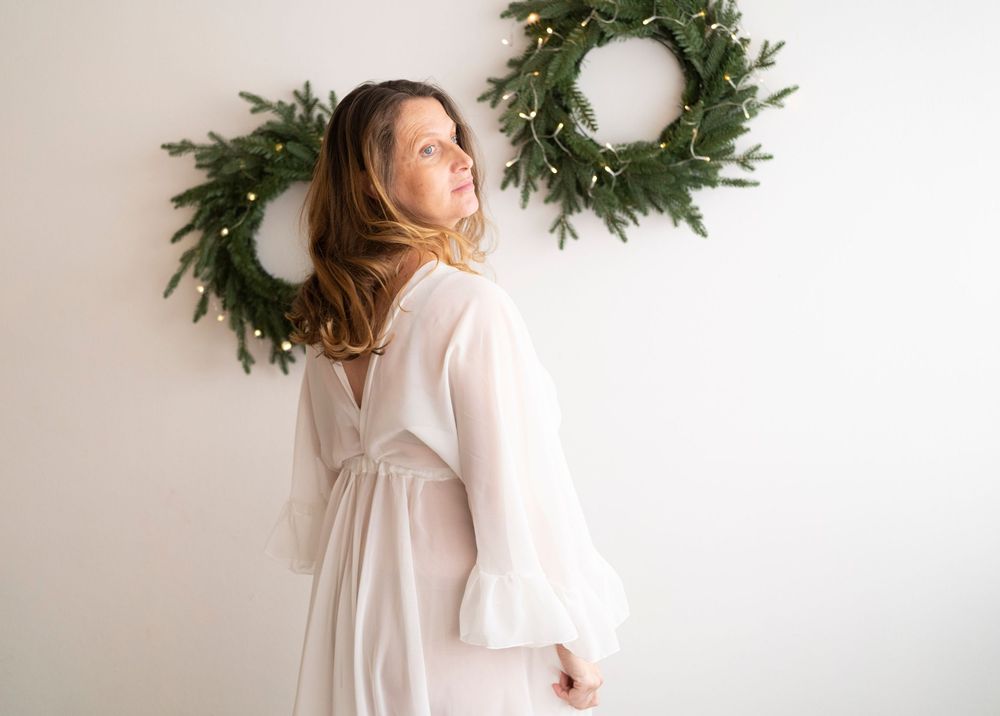 donna in gravidanza vestito bianco lungo a Natale, spalle di donna incinta, sessione gravidanza, fotografa maternità, corone di natale luci
