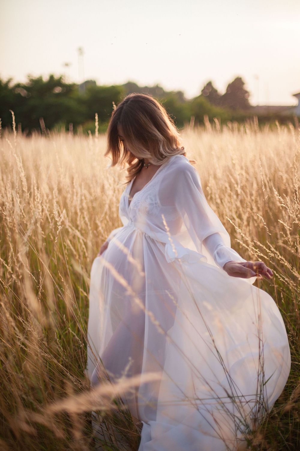 donna in gravidanza con vestito bianco al tramonto in un campo di spighe