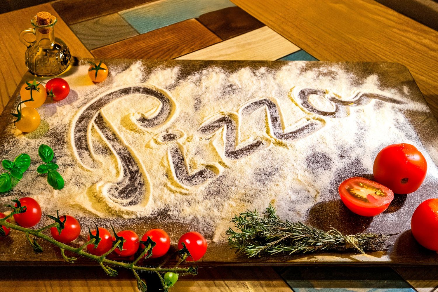 The word 'Pizza' written in flour on wooden surface with tomatoes and herbs.