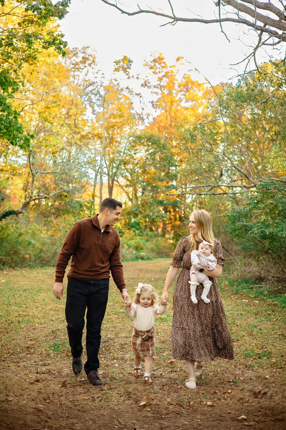 Family enjoying a fall day together in a wooded area with golden autumn leaves in the background.