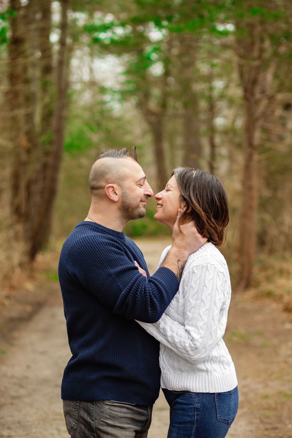 A romantic couple in matching sweaters share an intimate moment on a forest path during autumn.