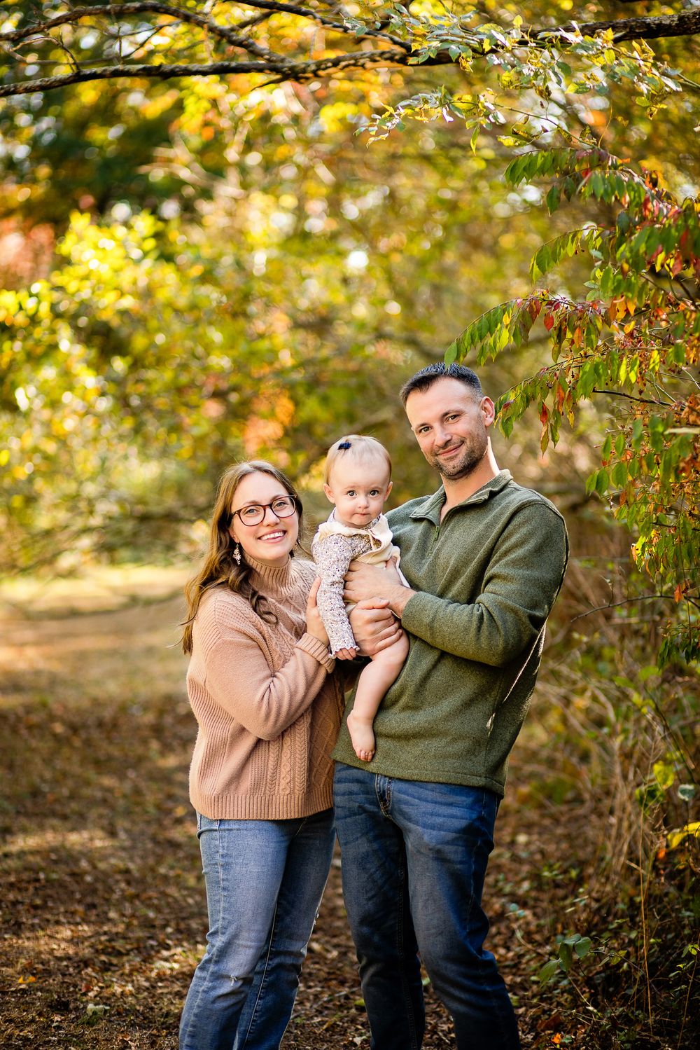 A small group poses together on an autumn path with golden leaves and sunlit foliage in the background.