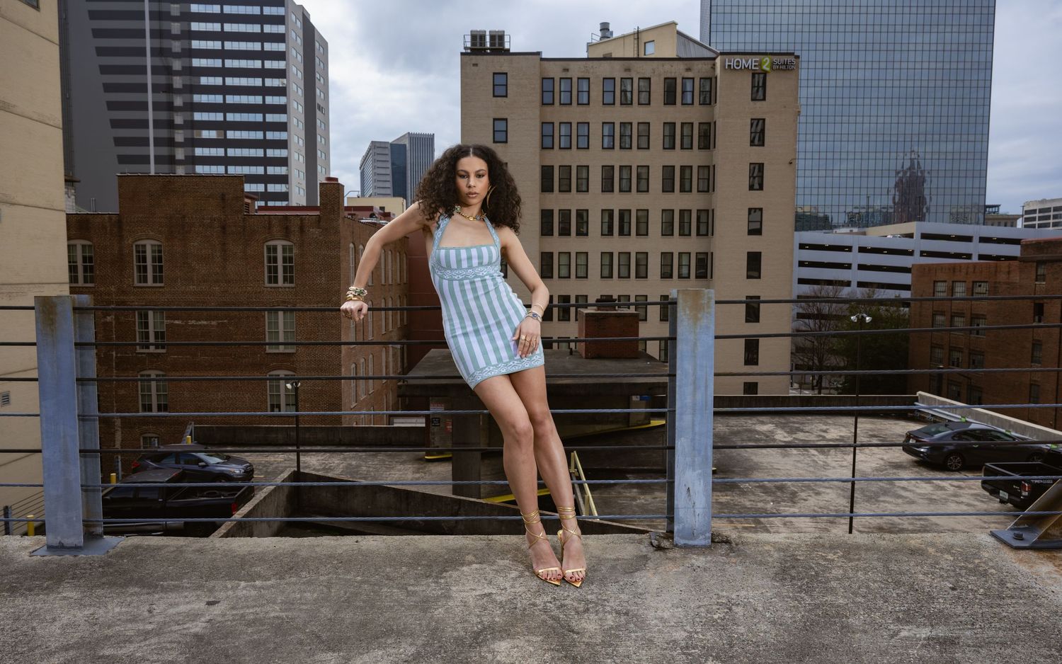 Rooftop fashion pose in blue striped outfit against city buildings.