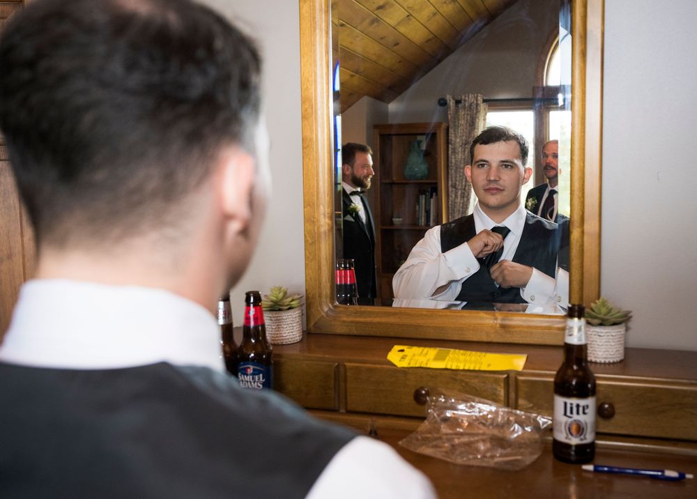 A formal dressed person adjusts their tie while looking in a mirror at a wooden vanity.