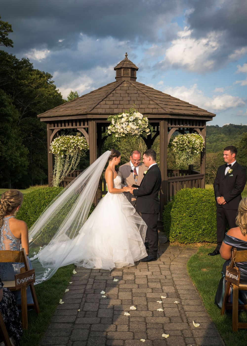 Wedding ceremony setup with gazebo decorated with white flowers and stone pathway.