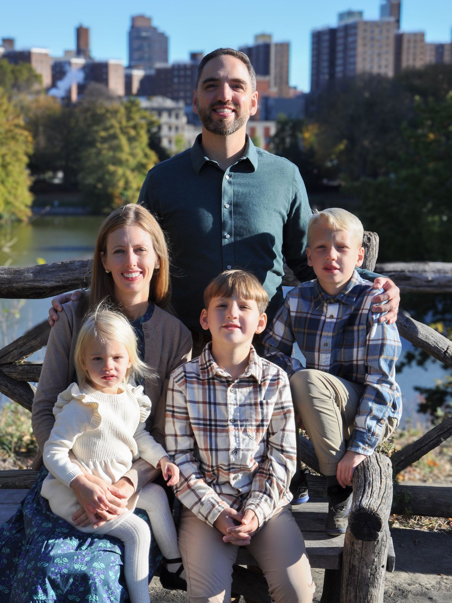 A posed family session at Harlem Meer in Central Park, NYC, featuring natural expressions and a mix of personalities against the skyline.