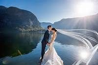 Couple in wedding attire share romantic moment by scenic mountain lake with sunlight bursting through dramatic veil.
