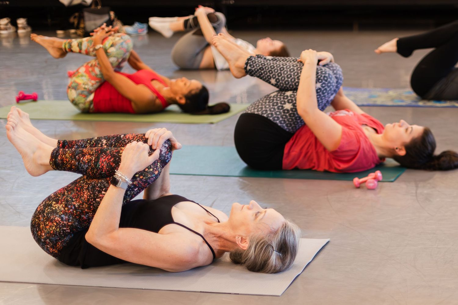 Dancers stretch on blue mats during a group exercise class performing core strengthening movements on the floor.