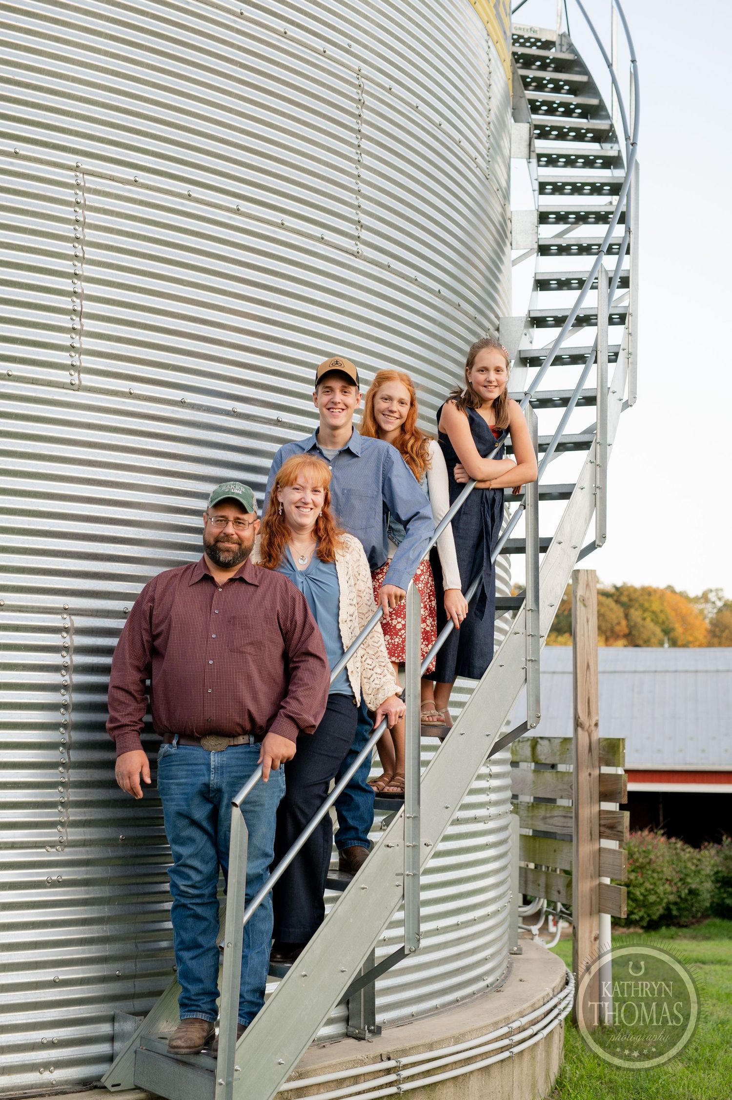 Group posed on metal stairs of a grain silo with red barn in the background.