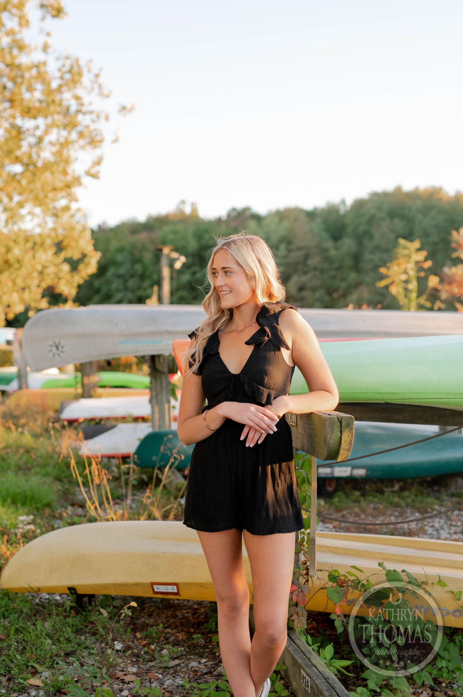 Person in black outfit standing by stored canoes during golden hour.
