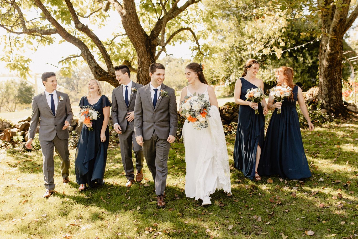 A wedding party walks together on a sunny autumn day with bridesmaids in navy dresses.