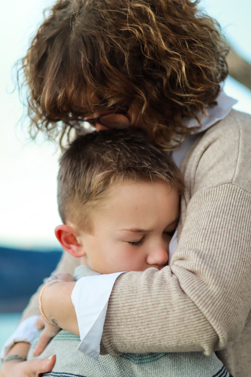 Intimate embrace between parent and child by water during sunset.