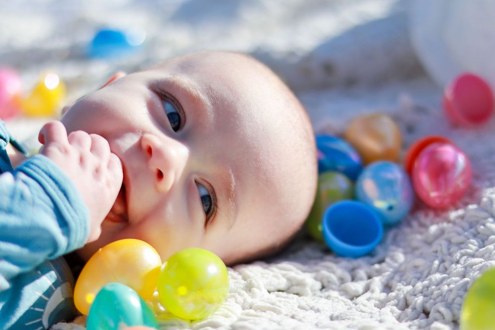 A baby lying on a blanket surrounded by colorful plastic balls smiles while playing.