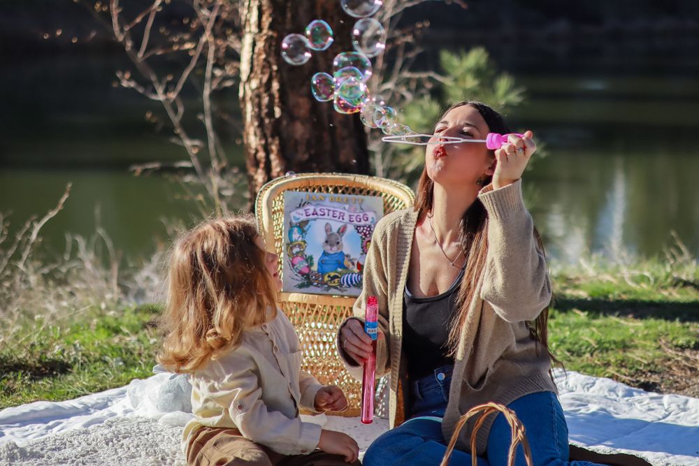 Two people relaxing outdoors by a lake on a blanket with a vintage-style illustrated poster between them.